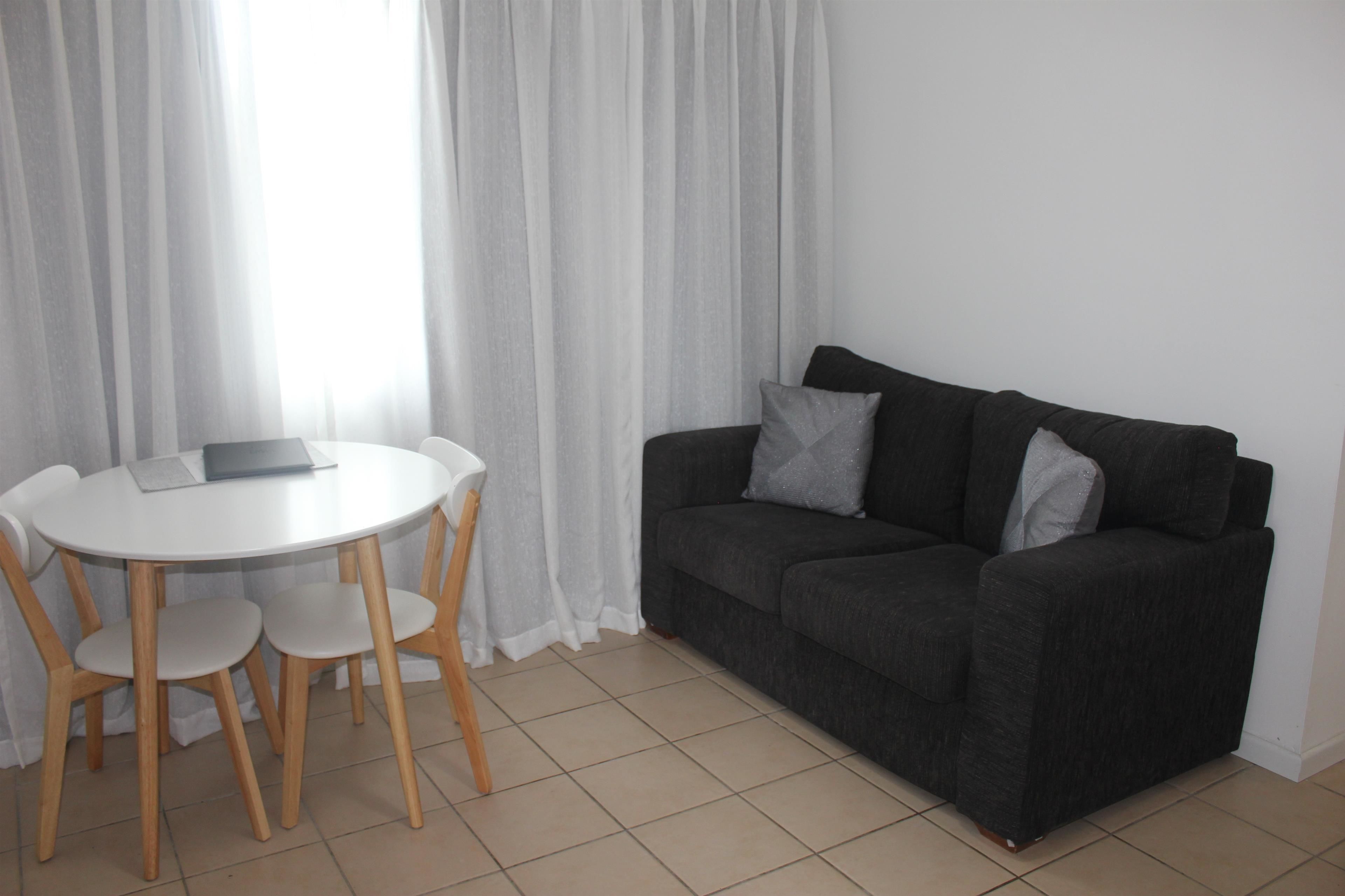 A living room with a dark grey sofa, two white chairs, a small round table, and a laptop on the table.