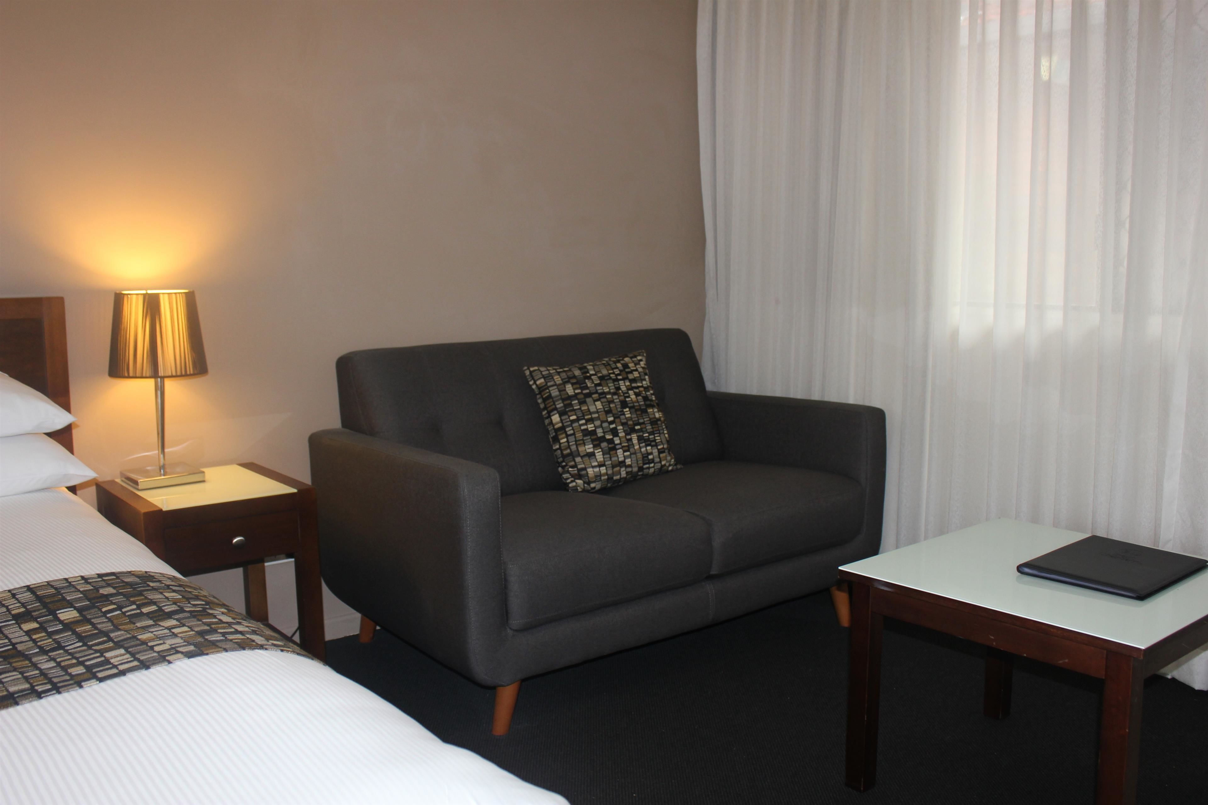 A hotel room with a bed, a sofa, a small table, a lamp, and a window with curtains.