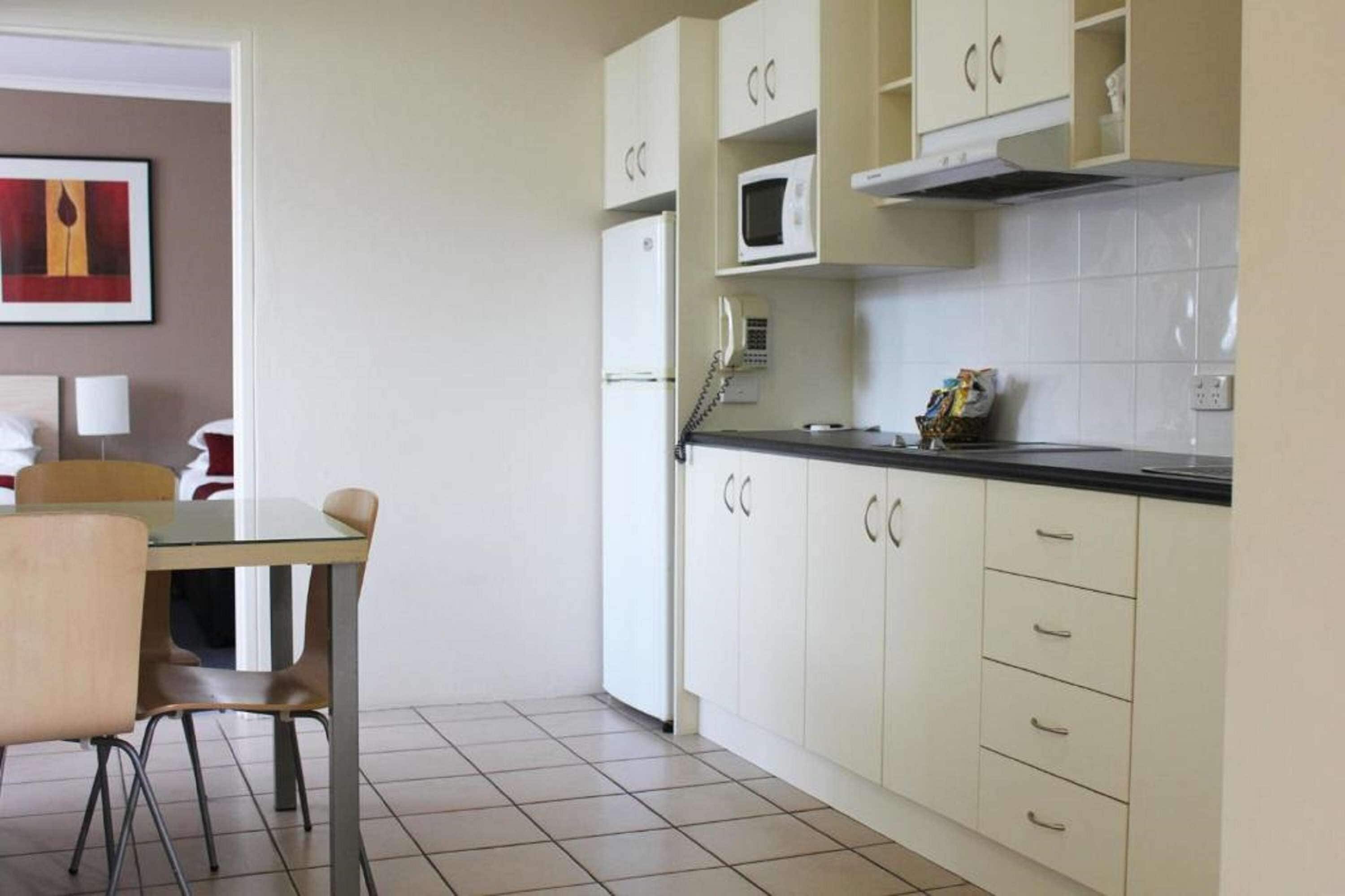 Cocina compacta con armarios blancos, un microondas y un teléfono. Hay una mesa de comedor con sillas.