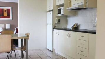Cocina compacta con armarios blancos, un microondas y un teléfono. Hay una mesa de comedor con sillas.