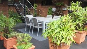 Un área de estar al aire libre con una mesa y sillas, rodeada de plantas en macetas.