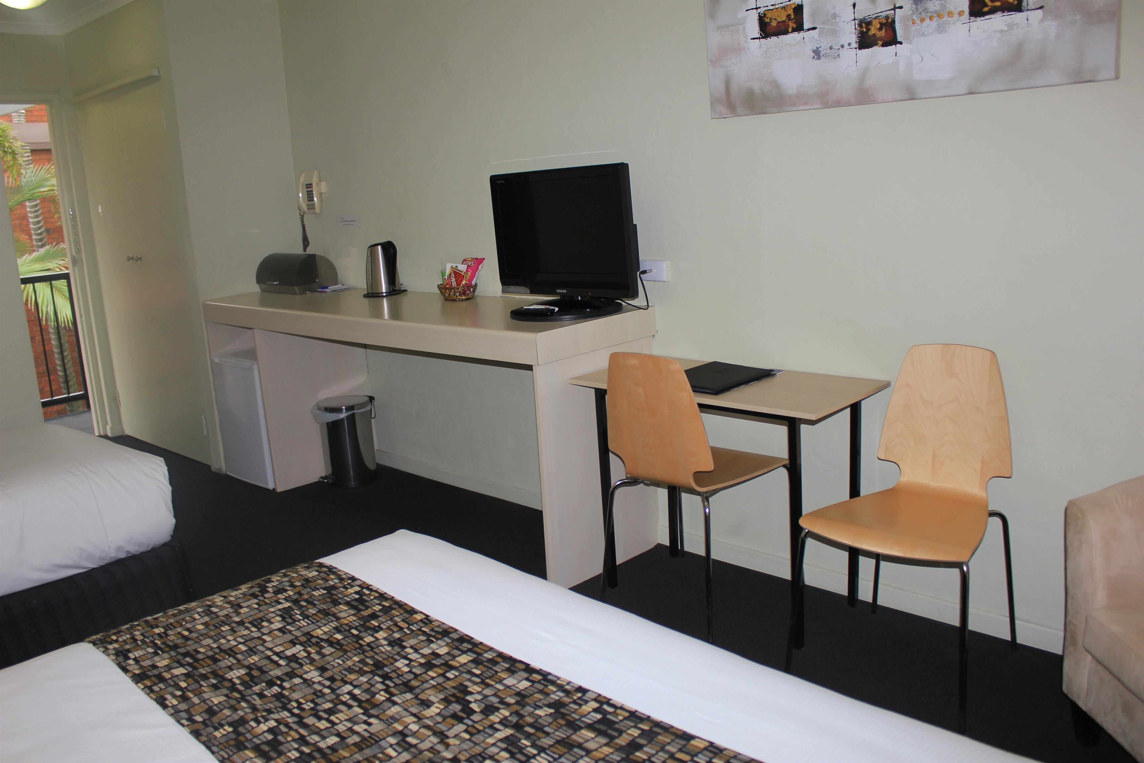 Una habitación de hotel con cama, escritorio con computadora, dos sillas y un cesto de basura.