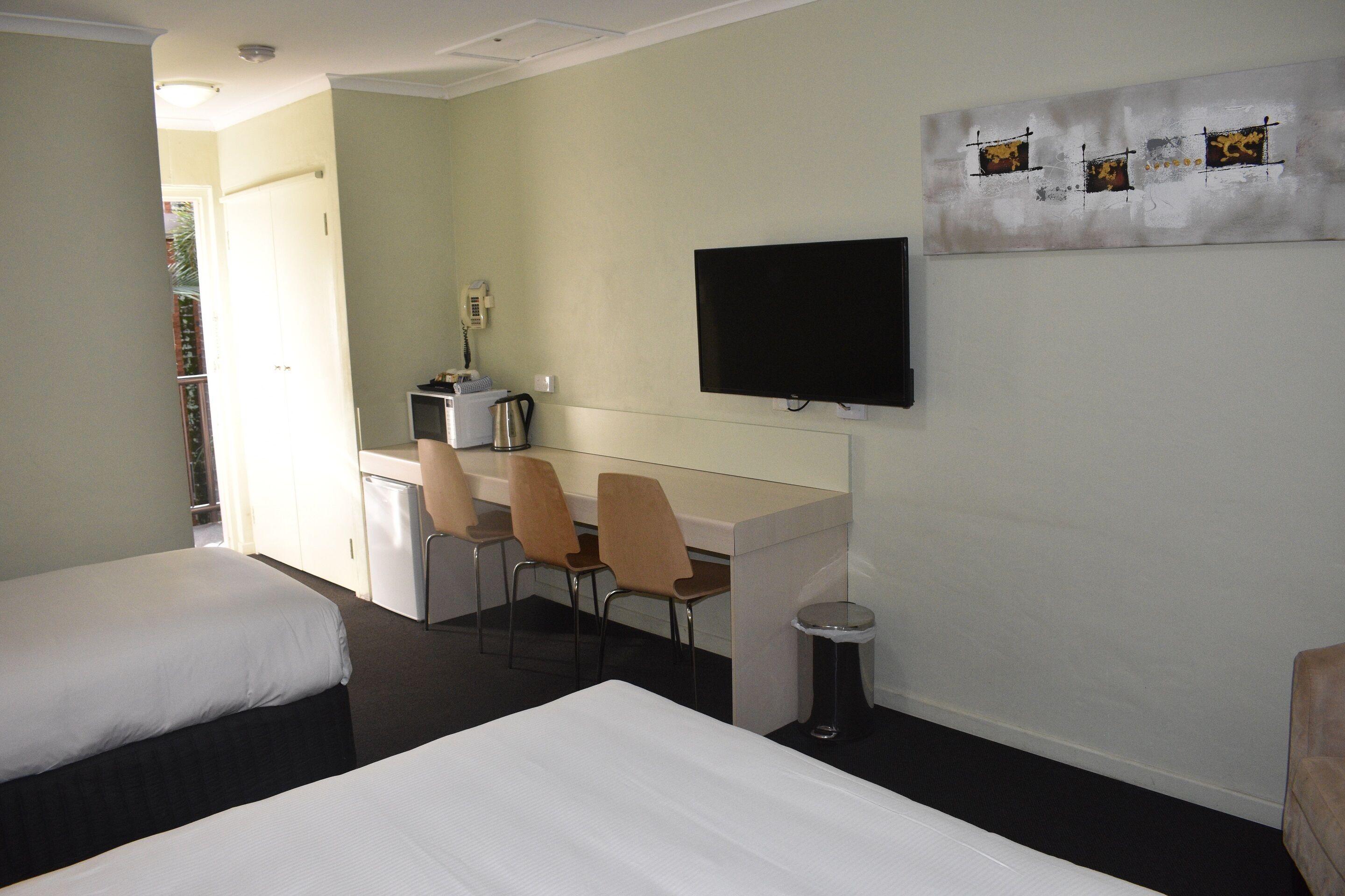 Habitación de hotel con dos camas, un escritorio con sillas, un televisor y una mesita.