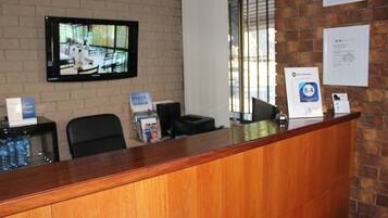A reception desk with a wooden counter, a television mounted on the wall, and a window with blinds.