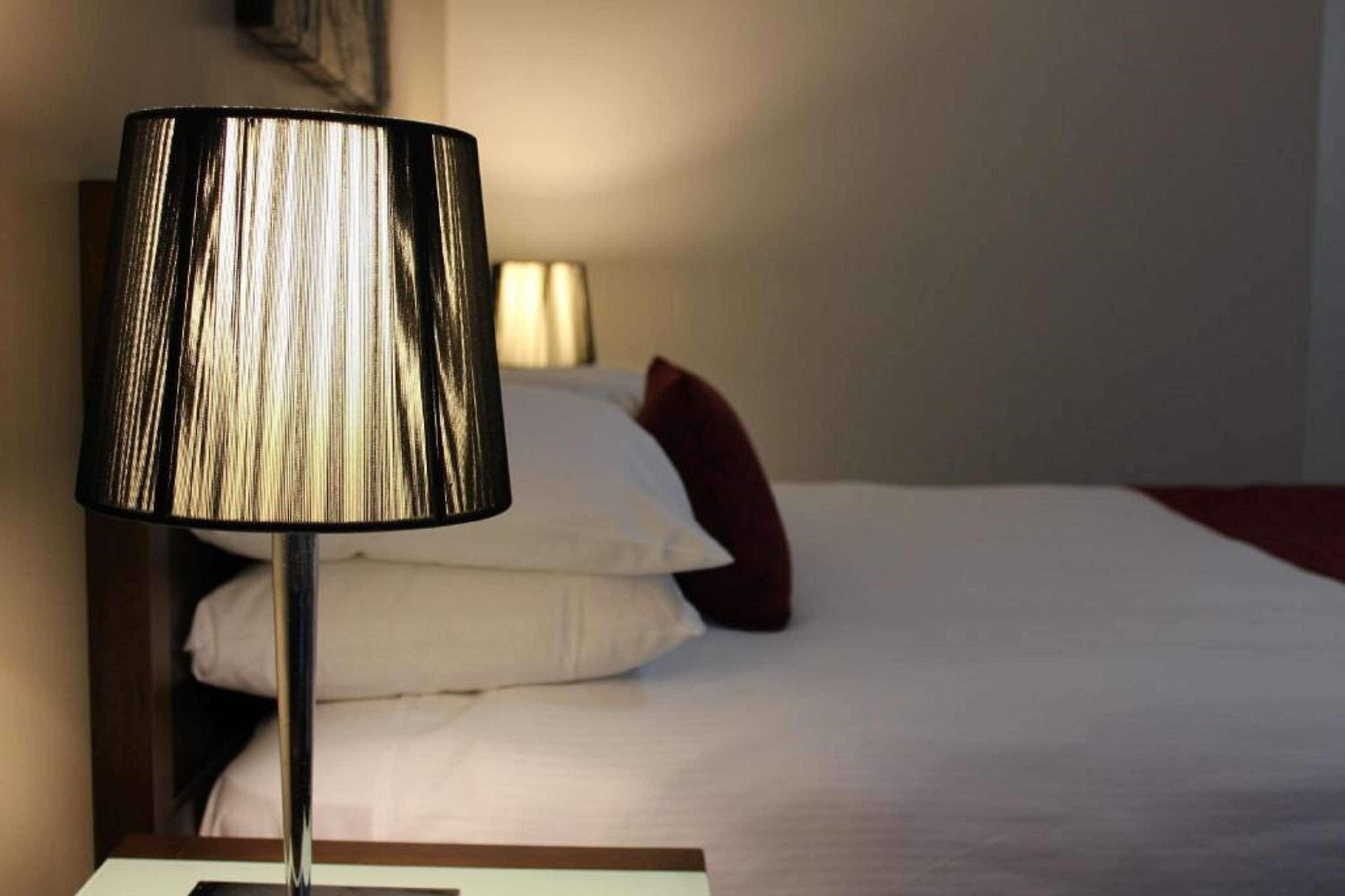 Ein Bett mit weißer Bettwäsche und einer schwarzen Nachttischlampe.
