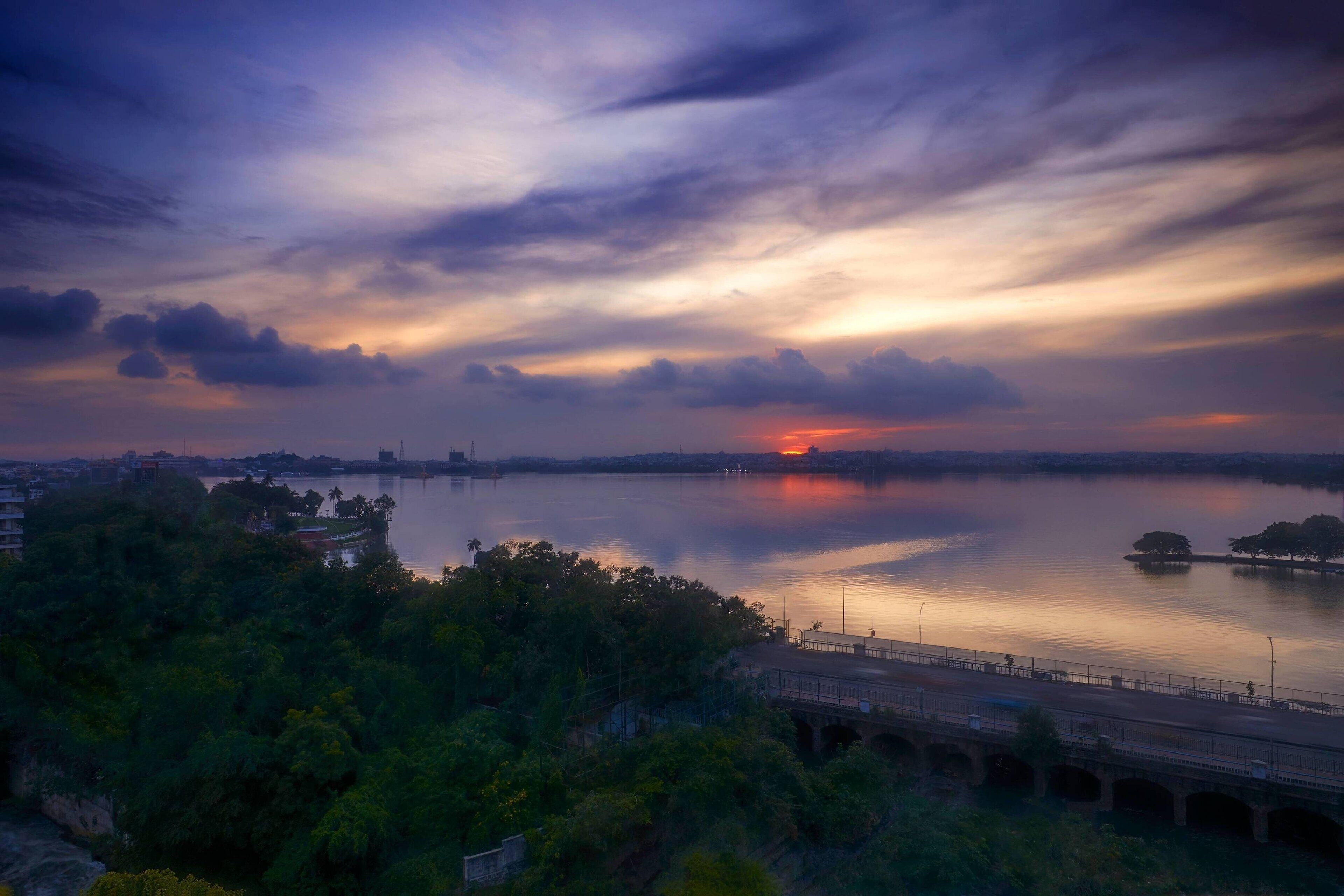Un coucher de soleil sur une rivière paisible, avec un pont au premier plan.