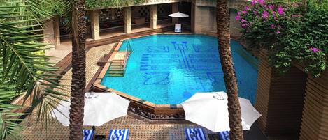 Una piscina con solárium de azulejos, palmeras y sillas de descanso.
