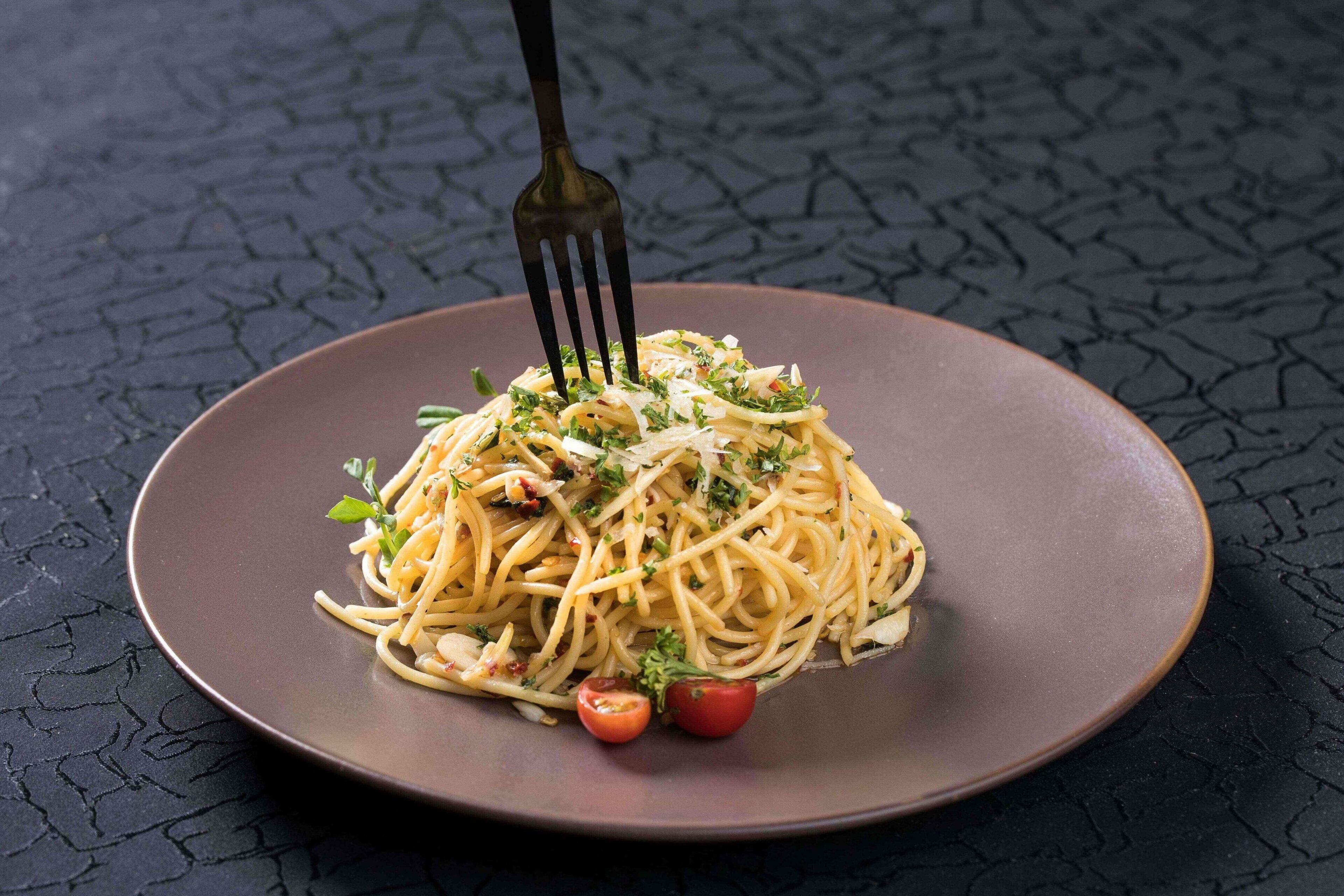 Eine Portion Spaghetti mit Kirschtomaten und Kräutern auf einem dunklen Teller.