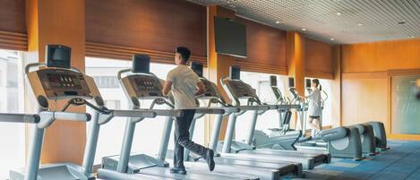 A gym with treadmills and a large screen on the wall.