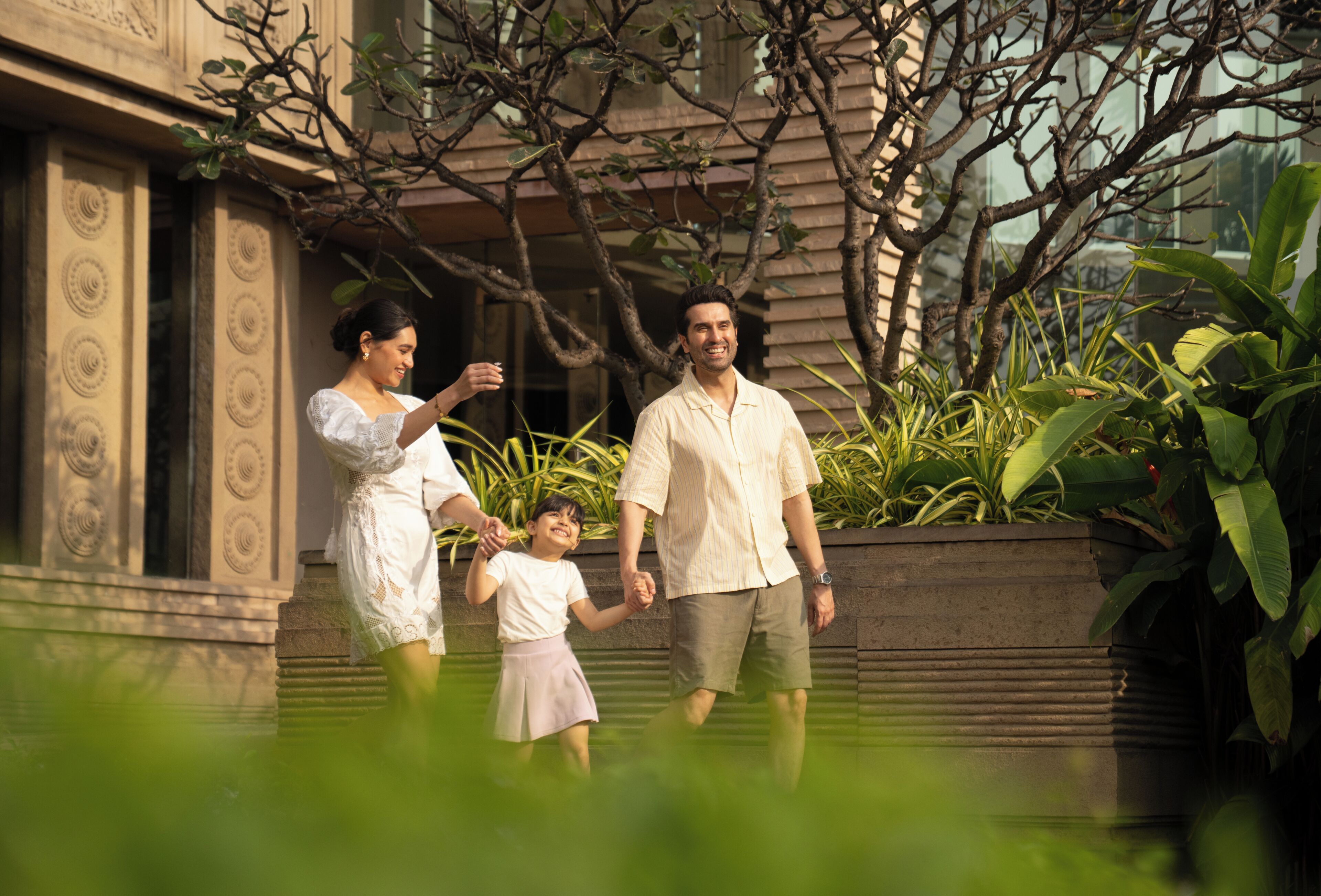 Una familia caminando por un sendero con un edificio y plantas al fondo.