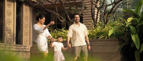 A family walking on a pathway with a building and plants in the background.