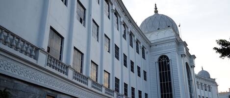 Un edificio grande y blanco con una cúpula y columnas, con numerosas ventanas y un balcón decorativo.