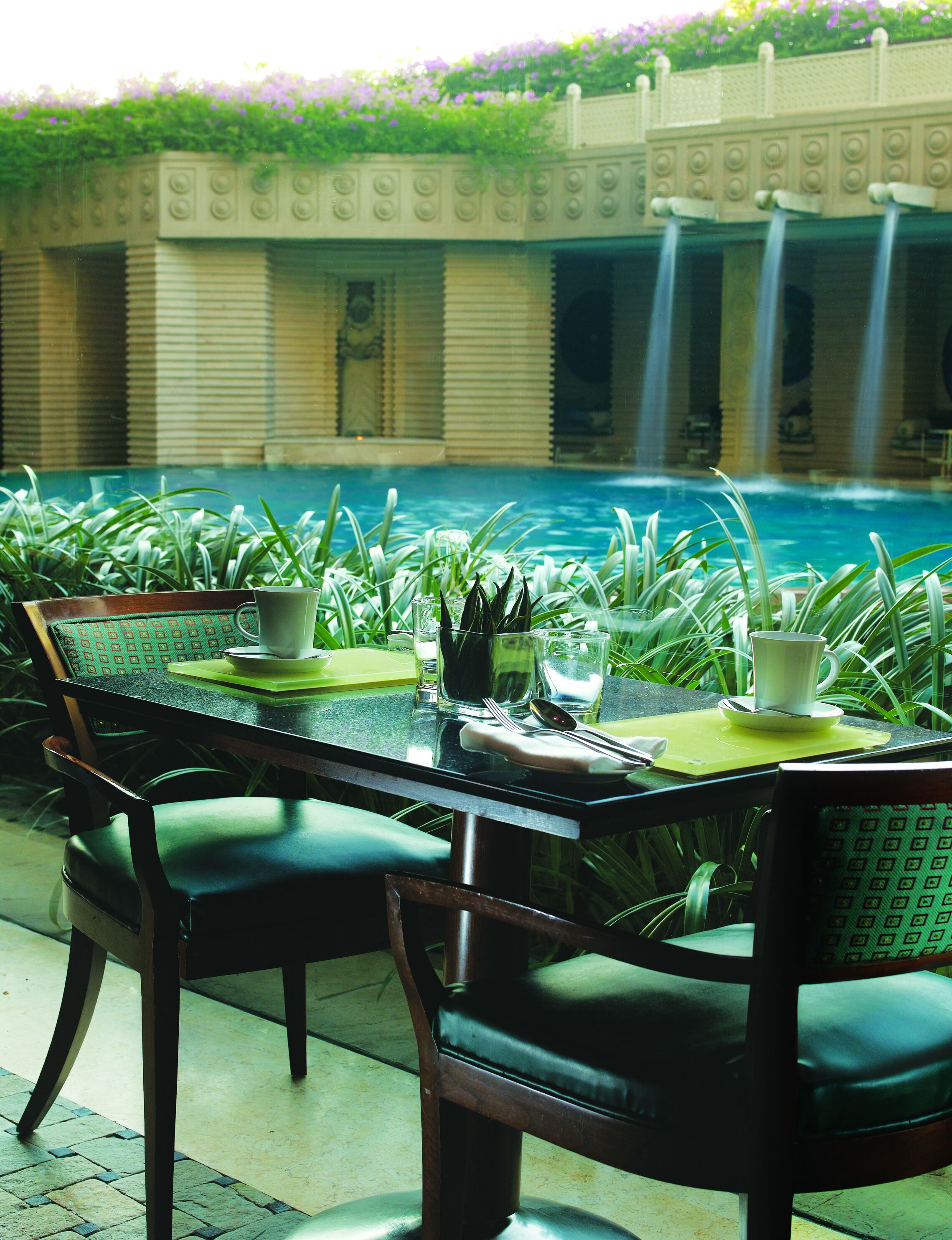 Une table à manger avec des chaises, donnant sur une piscine avec des cascades en arrière-plan.