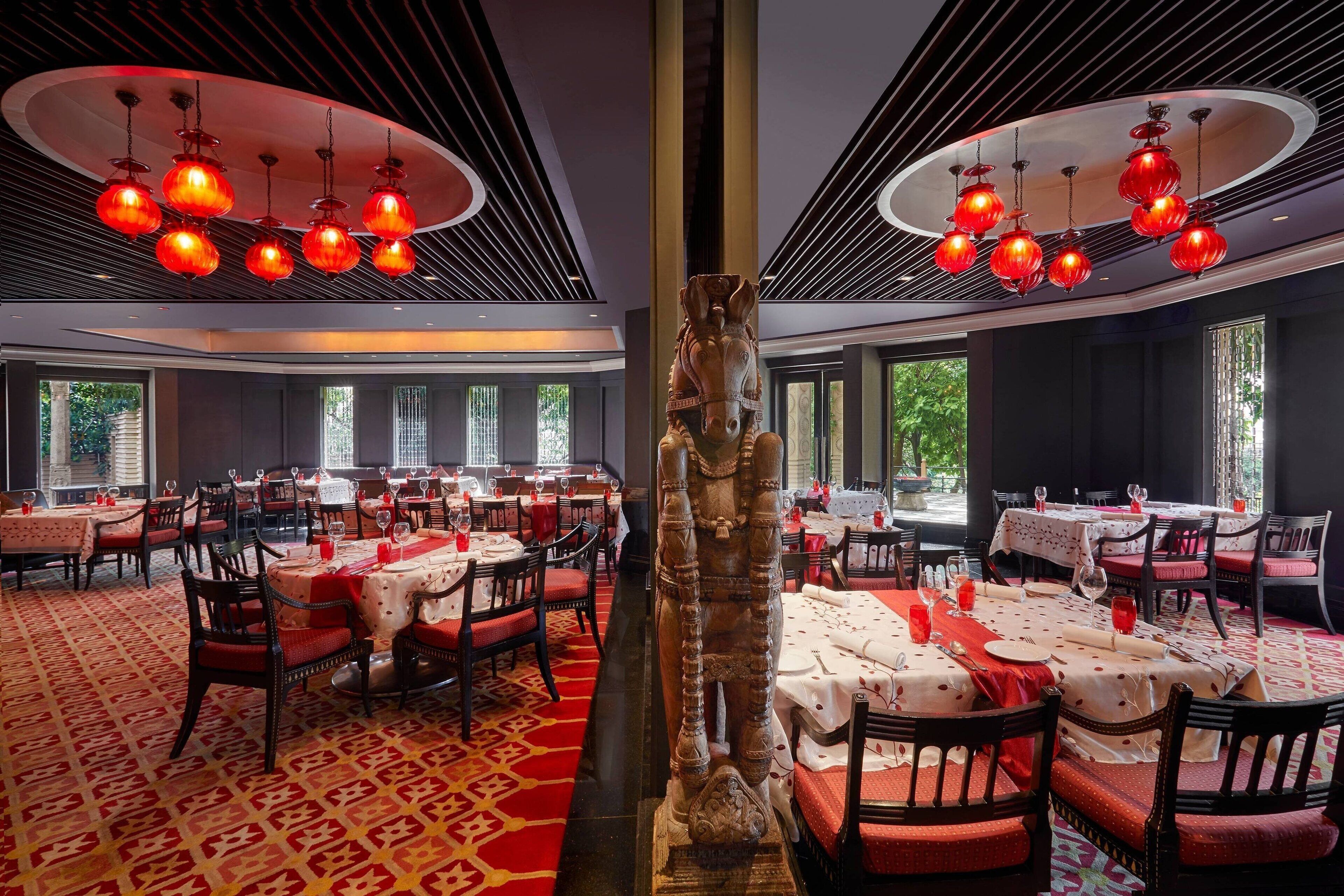 A restaurant with round tables, red chairs, and a central statue.