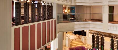 Un vestíbulo de hotel de varios niveles con una zona de estar central, varios balcones y una imponente escalera.