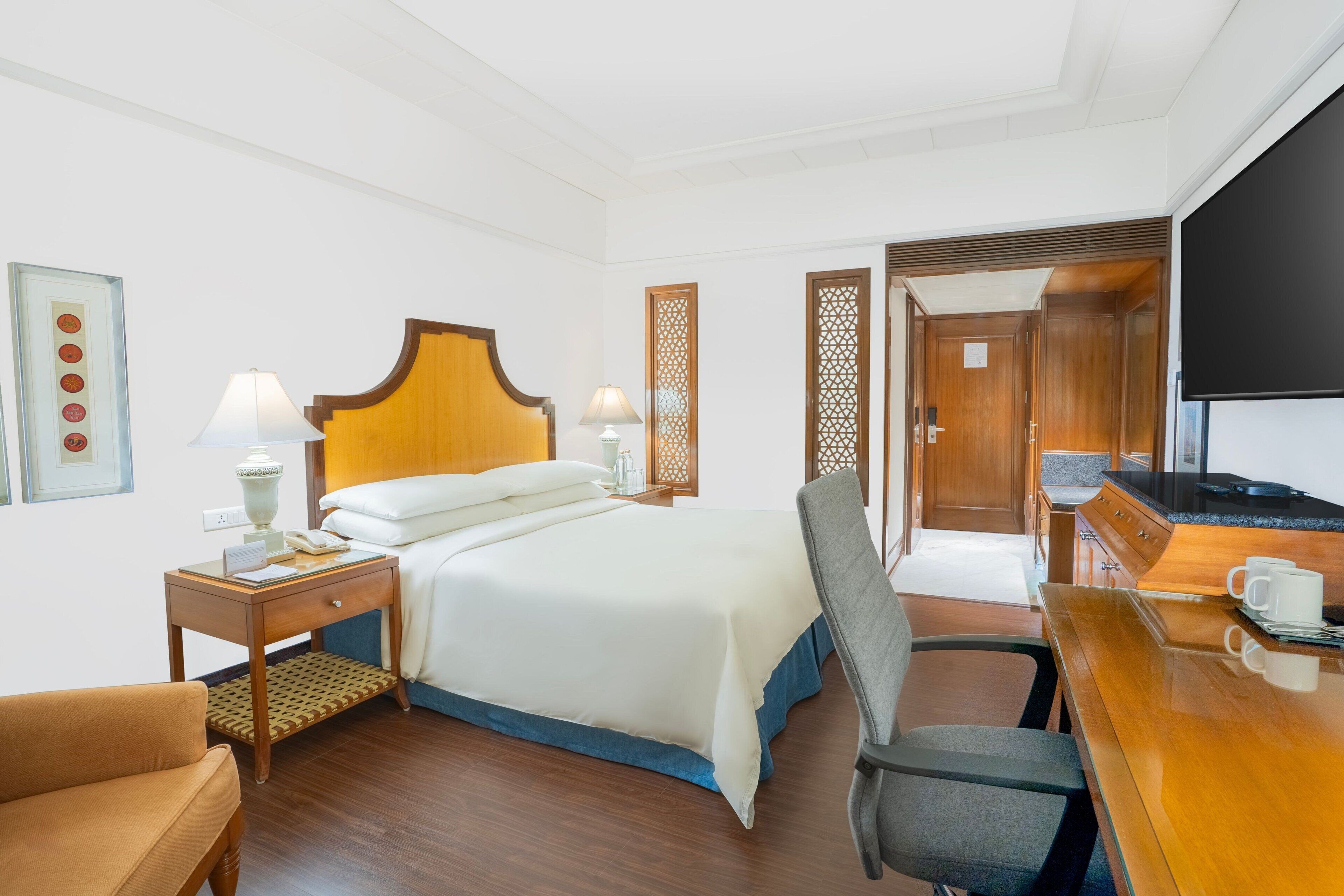 Ein Hotelzimmer mit einem Bett, einem Schreibtisch, einem Sessel, einem Fernseher und einem Holzschrank.
