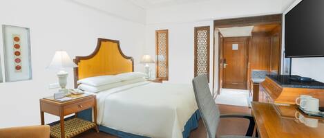 A hotel room with a bed, a desk, a chair, a TV, and a wooden wardrobe.