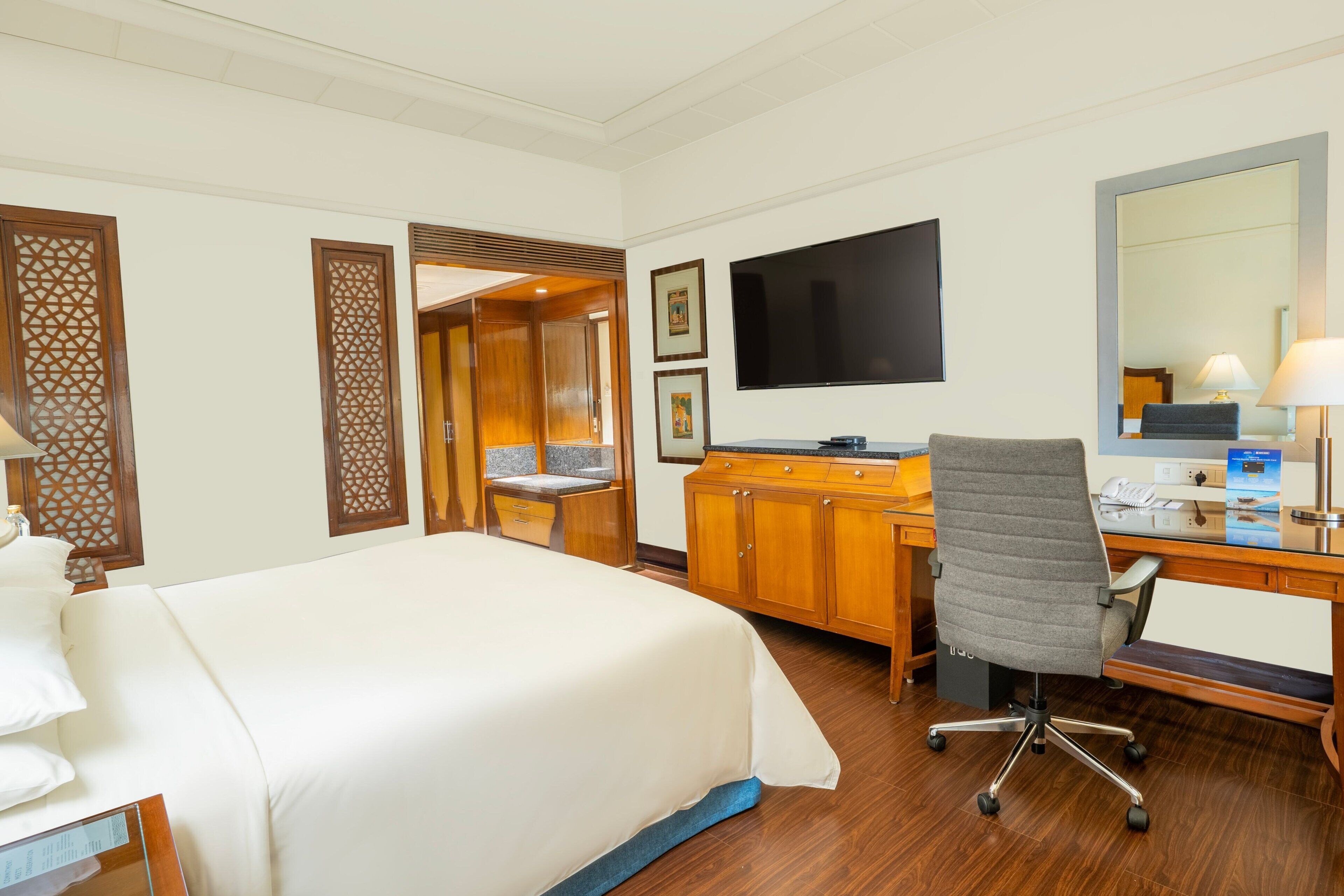 Una habitación de hotel con una cama grande, un escritorio de madera, una silla y un televisor.