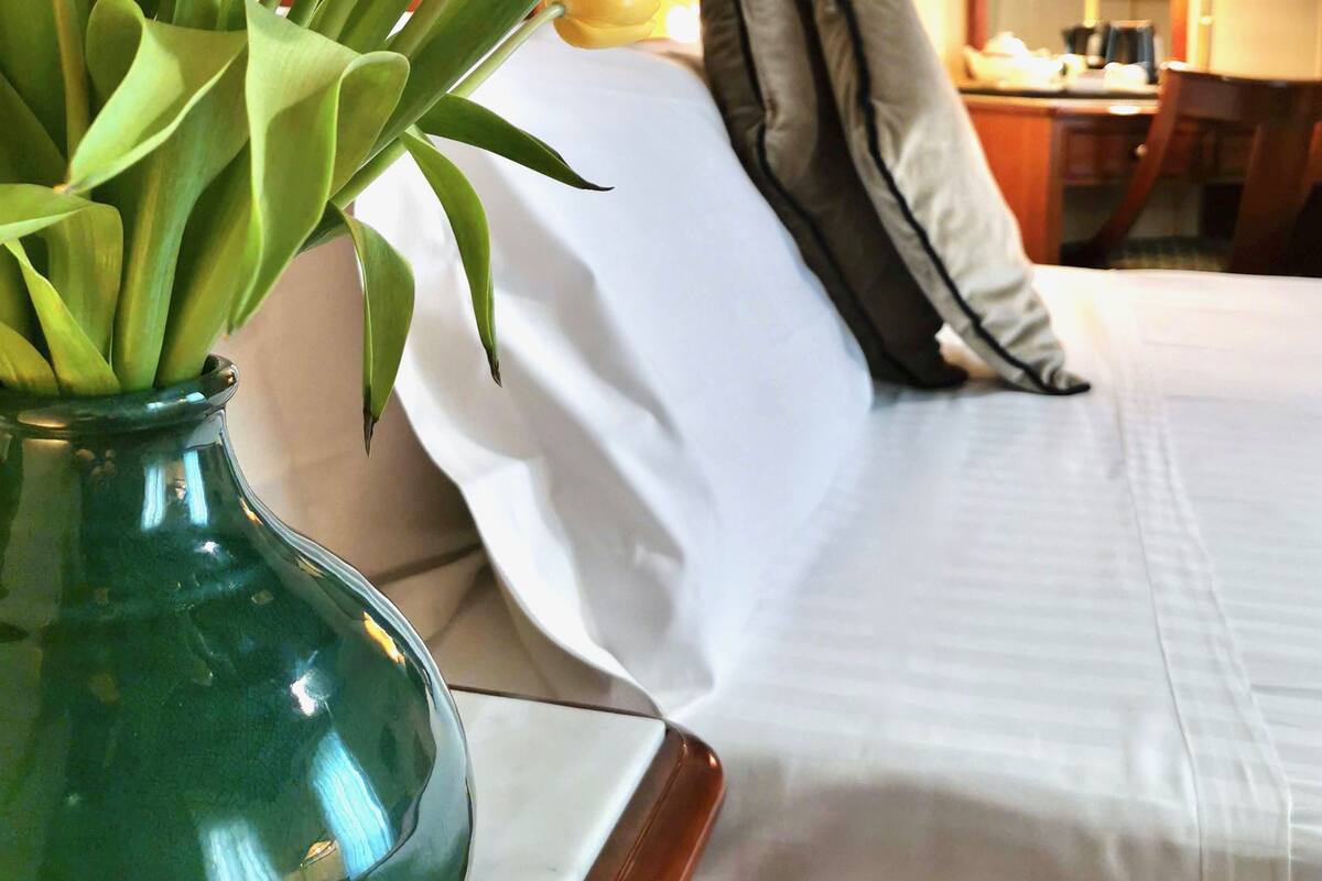 A hotel room with a bed, a nightstand, a lamp, and a vase with yellow tulips.