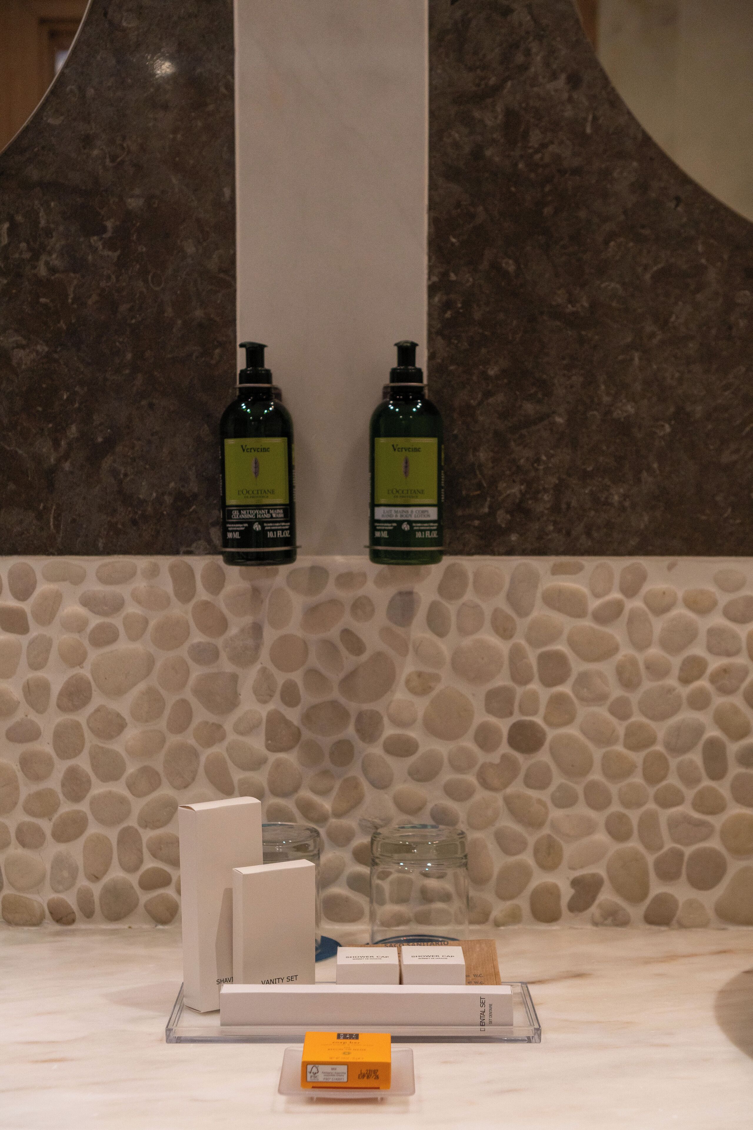 Ein Badezimmer mit einer Rückwand aus Steinmosaik, zwei Shampoo-Flaschen und einem Schminktisch.