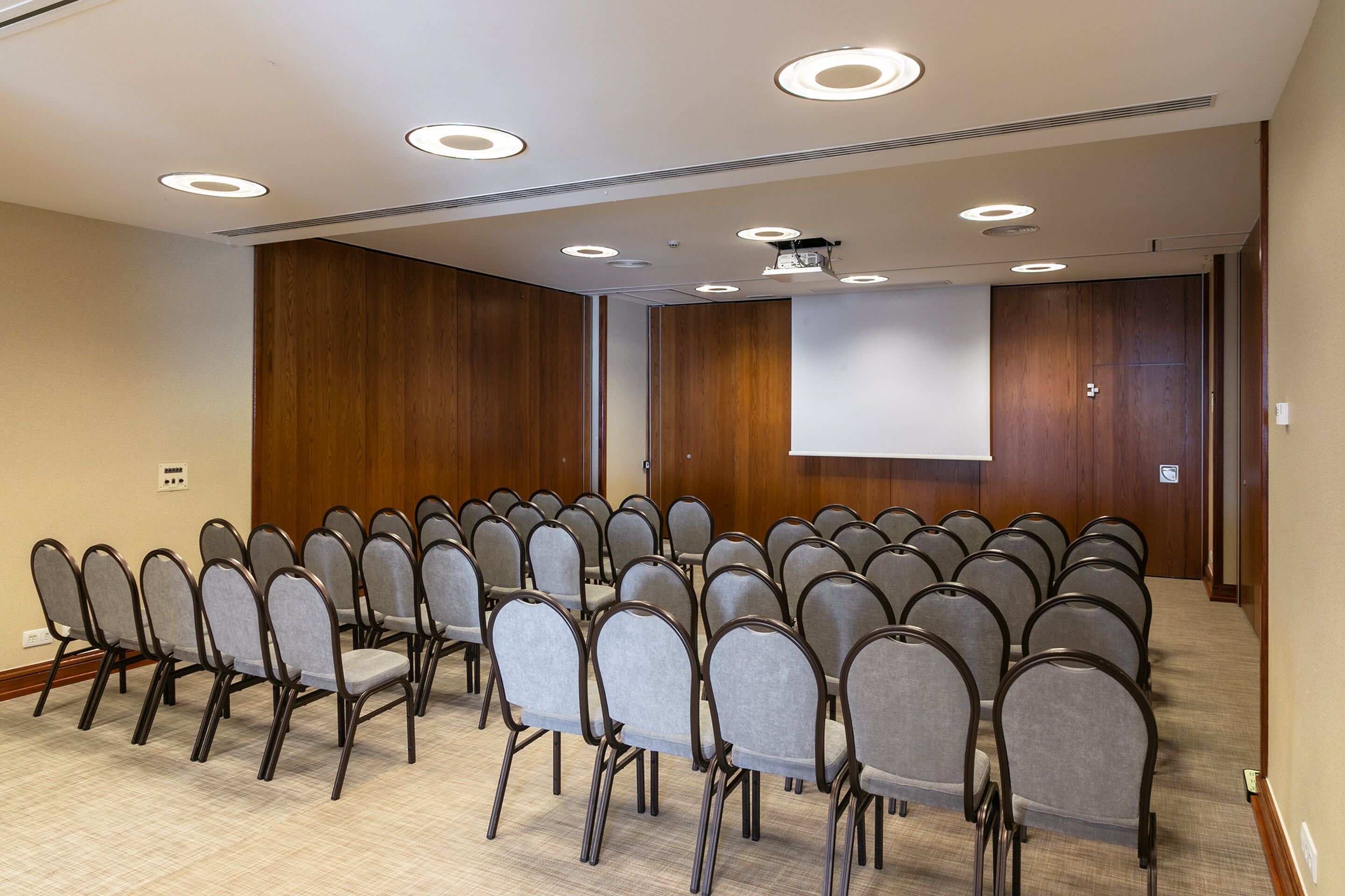 A conference room with rows of chairs, a projector screen, and wooden panel walls.