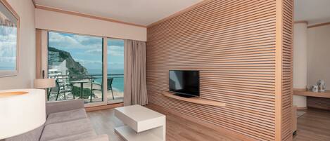 Un salón moderno con un televisor grande, un panel de pared de madera y un balcón con vistas al mar.