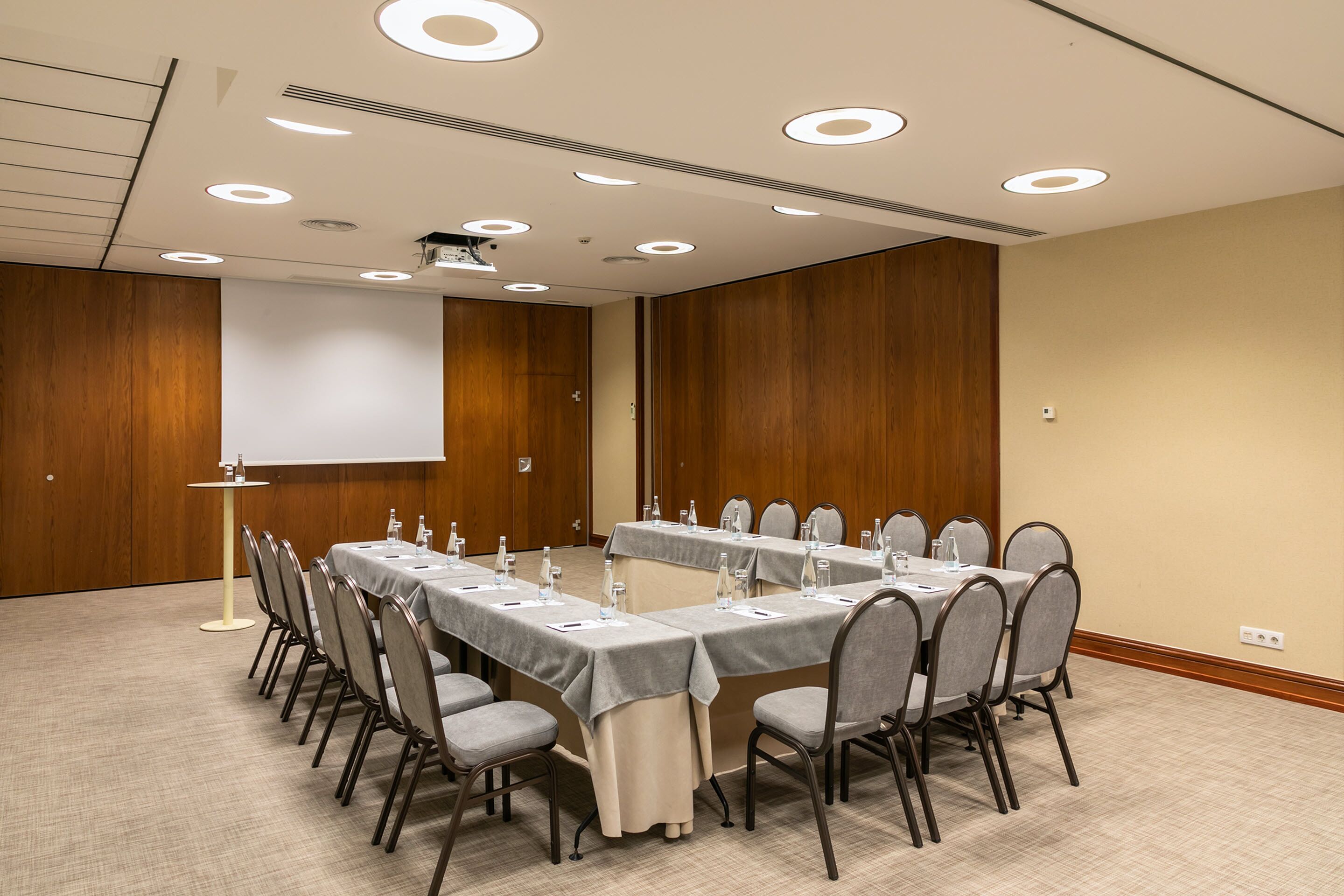 A conference room with two long tables, chairs, and a projector screen.