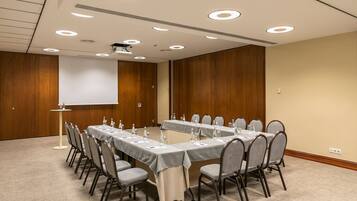 A conference room with two long tables, chairs, and a projector screen.