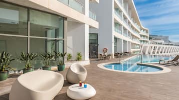 Een modern hotel met een zwembad, plantenpotten en lounge stoelen.