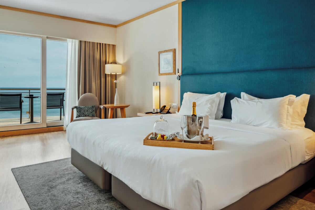 Ein Hotelzimmer mit einem großen Bett, Meerblick, einem Essbereich und einem Balkon.