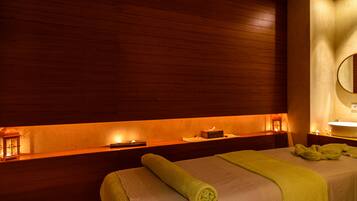 A hotel room with a wooden headboard, a bed with a green towel, a nightstand with a lamp, and a wall-mounted mirror.