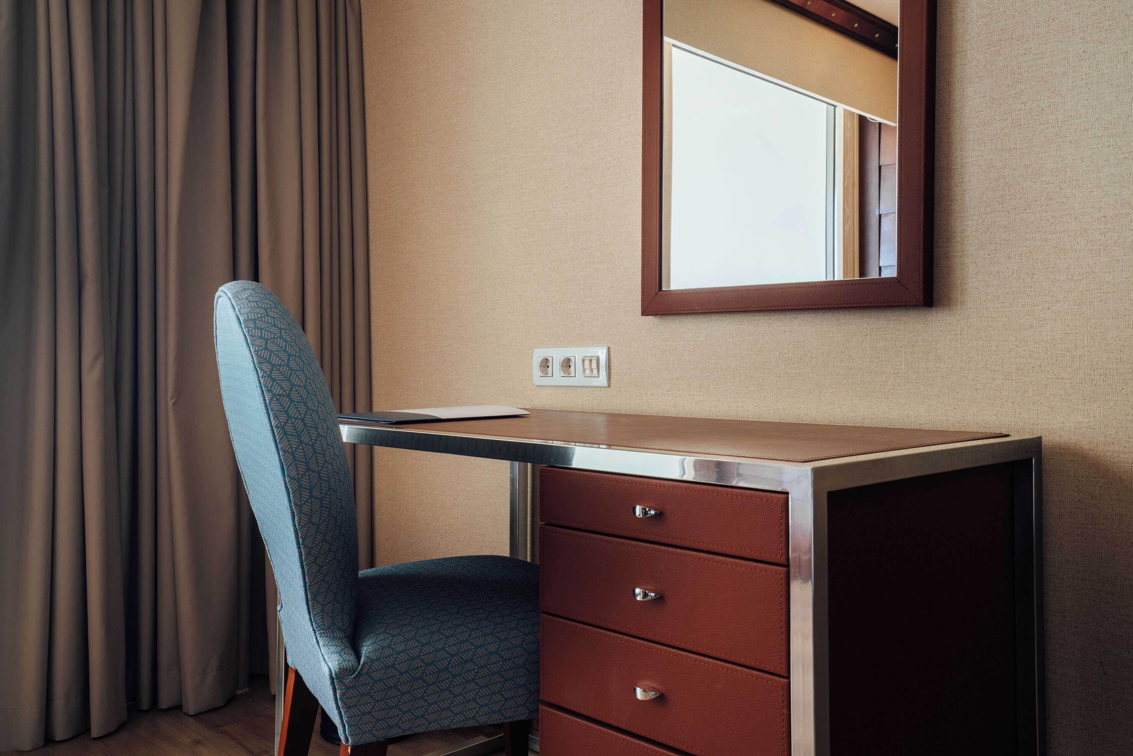 A hotel room with a desk, chair, and a mirror.