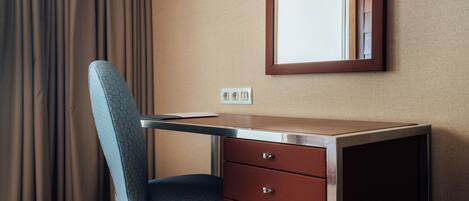 A hotel room with a desk, chair, and a mirror.