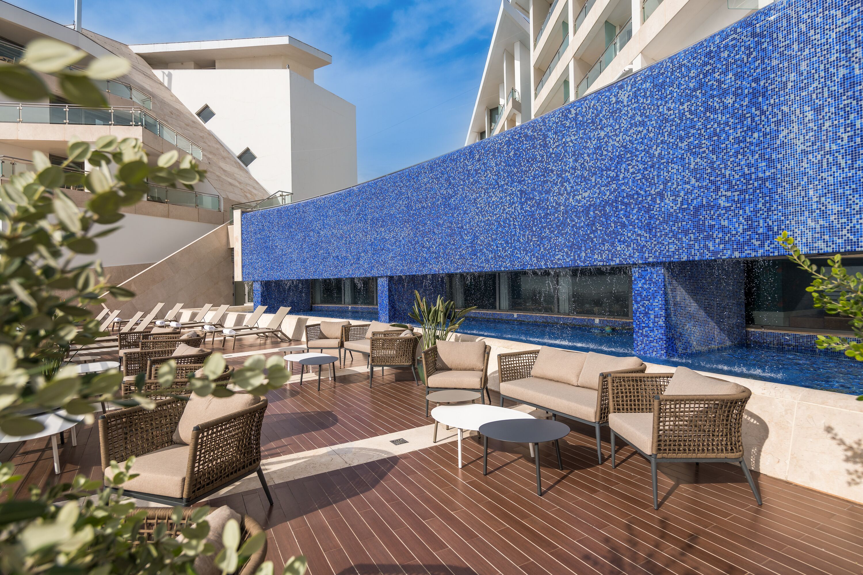 A rooftop terrace with outdoor seating, a pool, and a building with a blue mosaic facade.