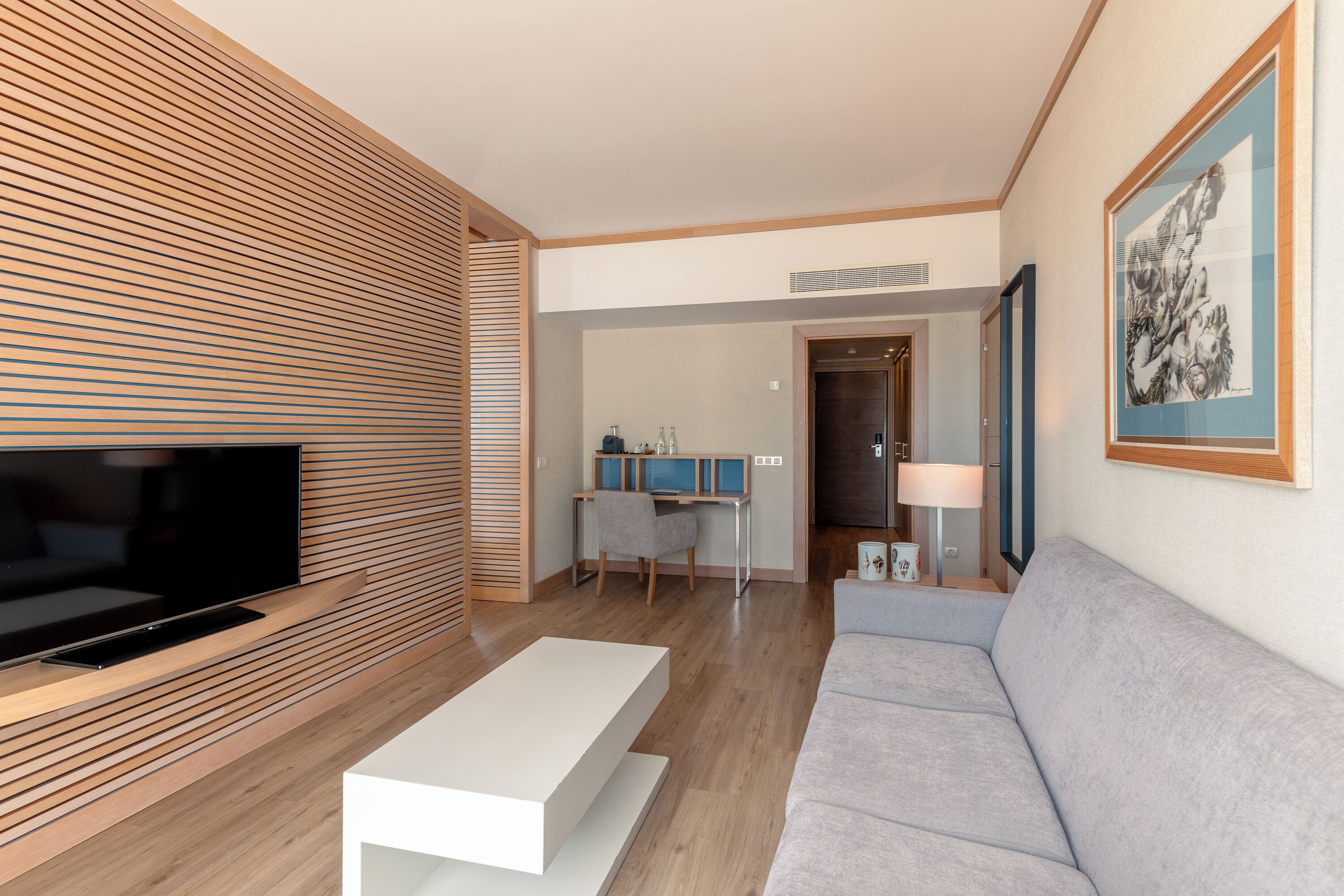 Una sala de estar moderna con un televisor de pantalla plana, una mesa de centro blanca, un sofá gris y una pared de listones de madera.