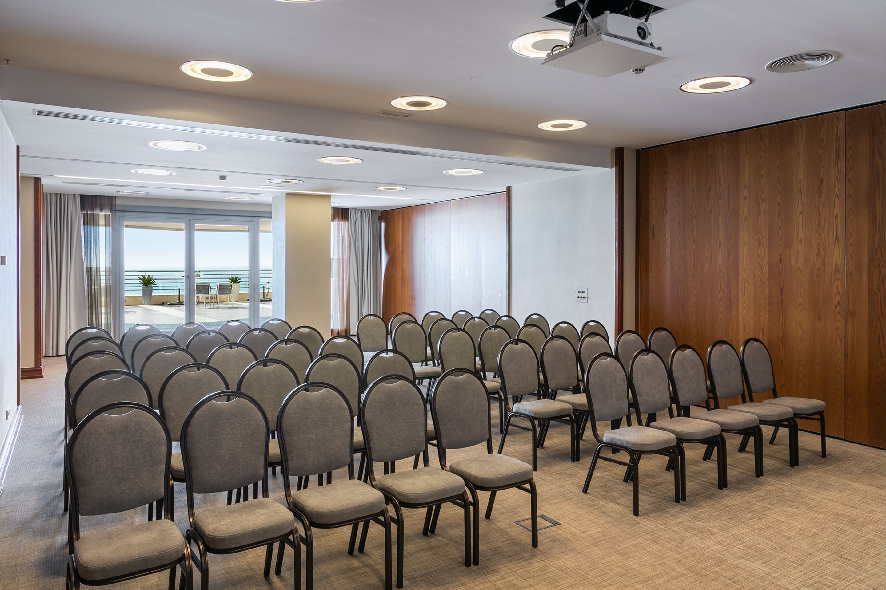 A conference room with rows of chairs, a projector, and a large window with a view of the ocean.
