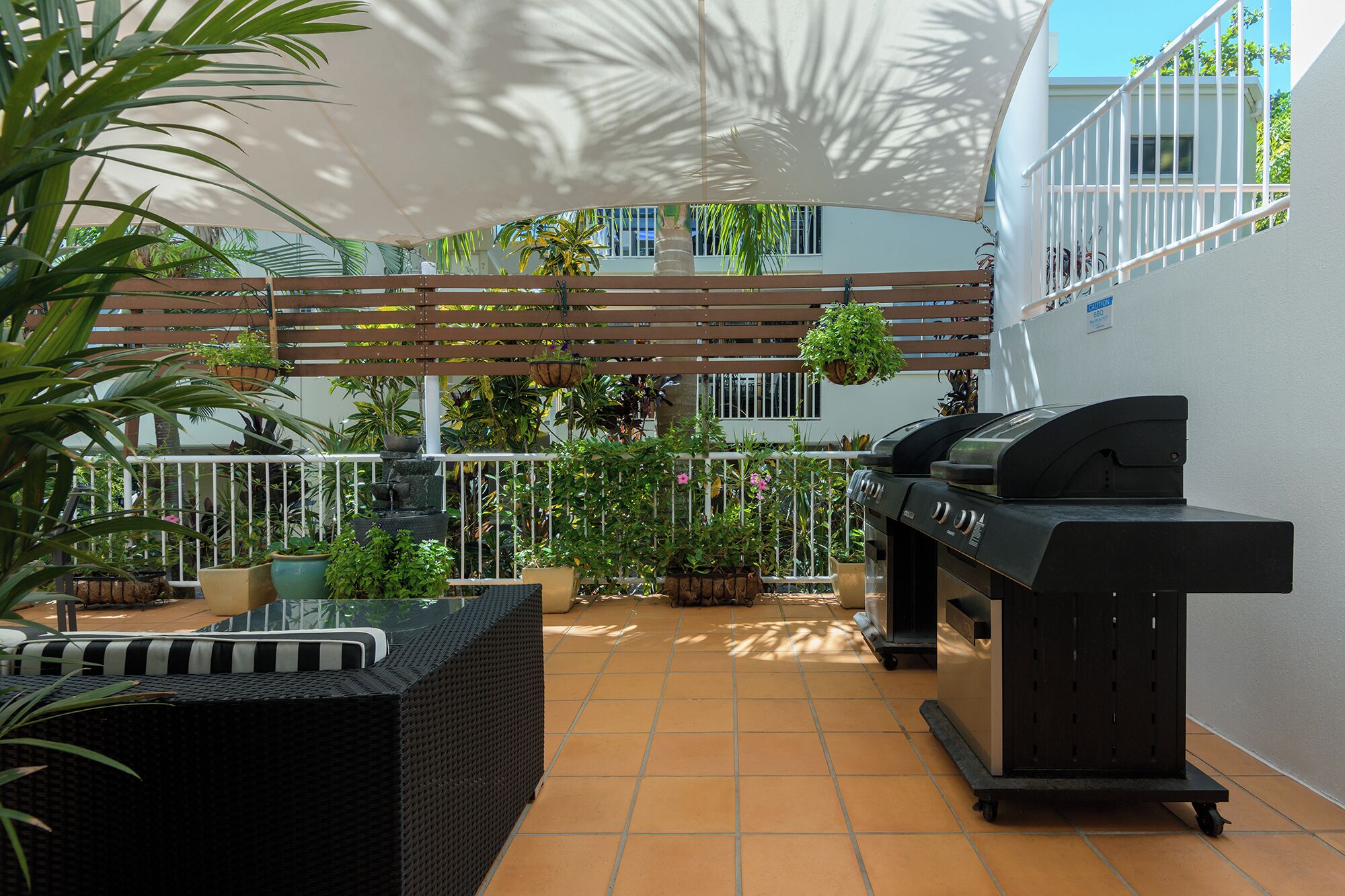 Una terrazza con barbecue, mobili in vimini, piante in vaso e un tettoia bianca.