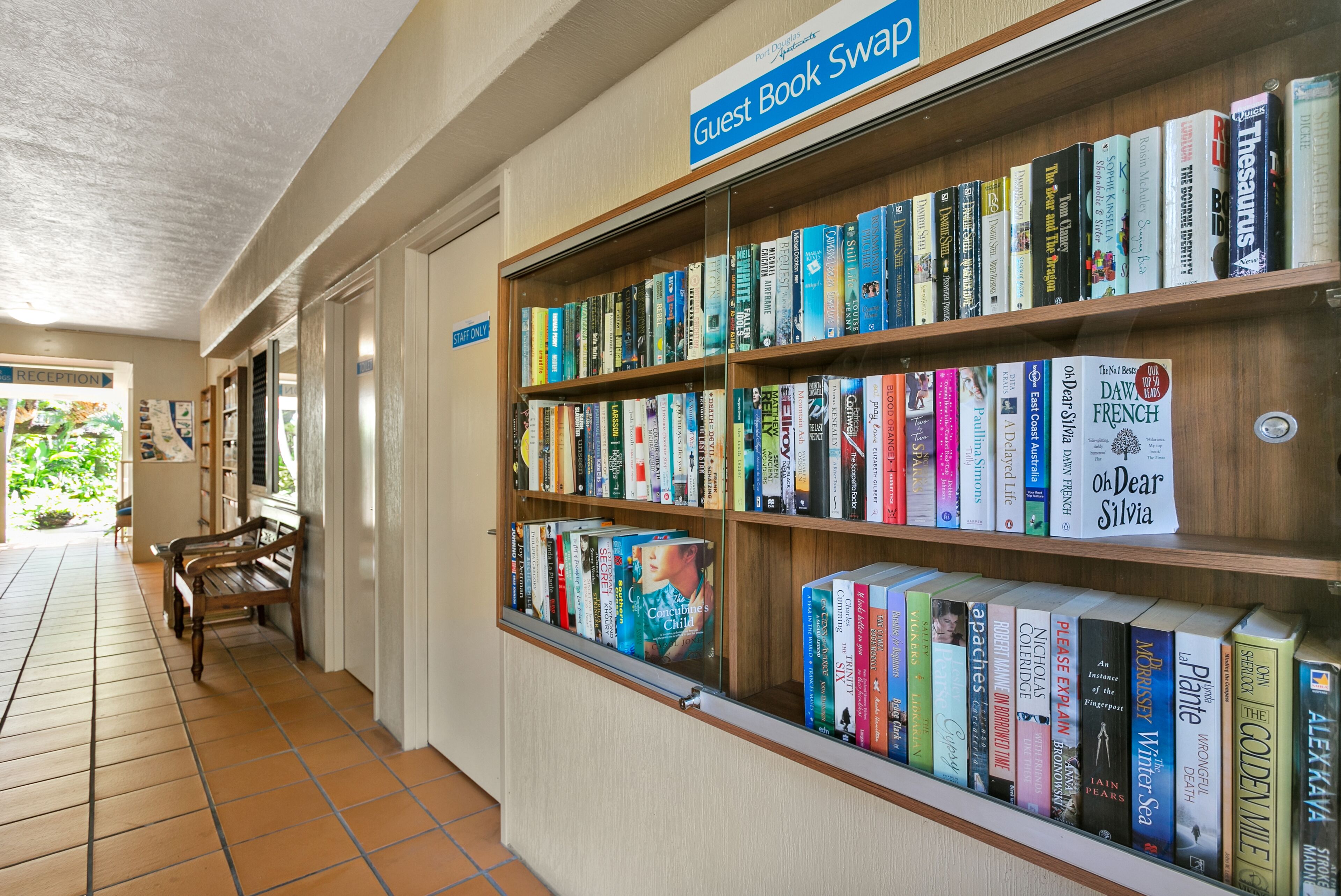 A library with a 'Guest Book Swap' sign, wooden bookshelves, and a tiled floor.