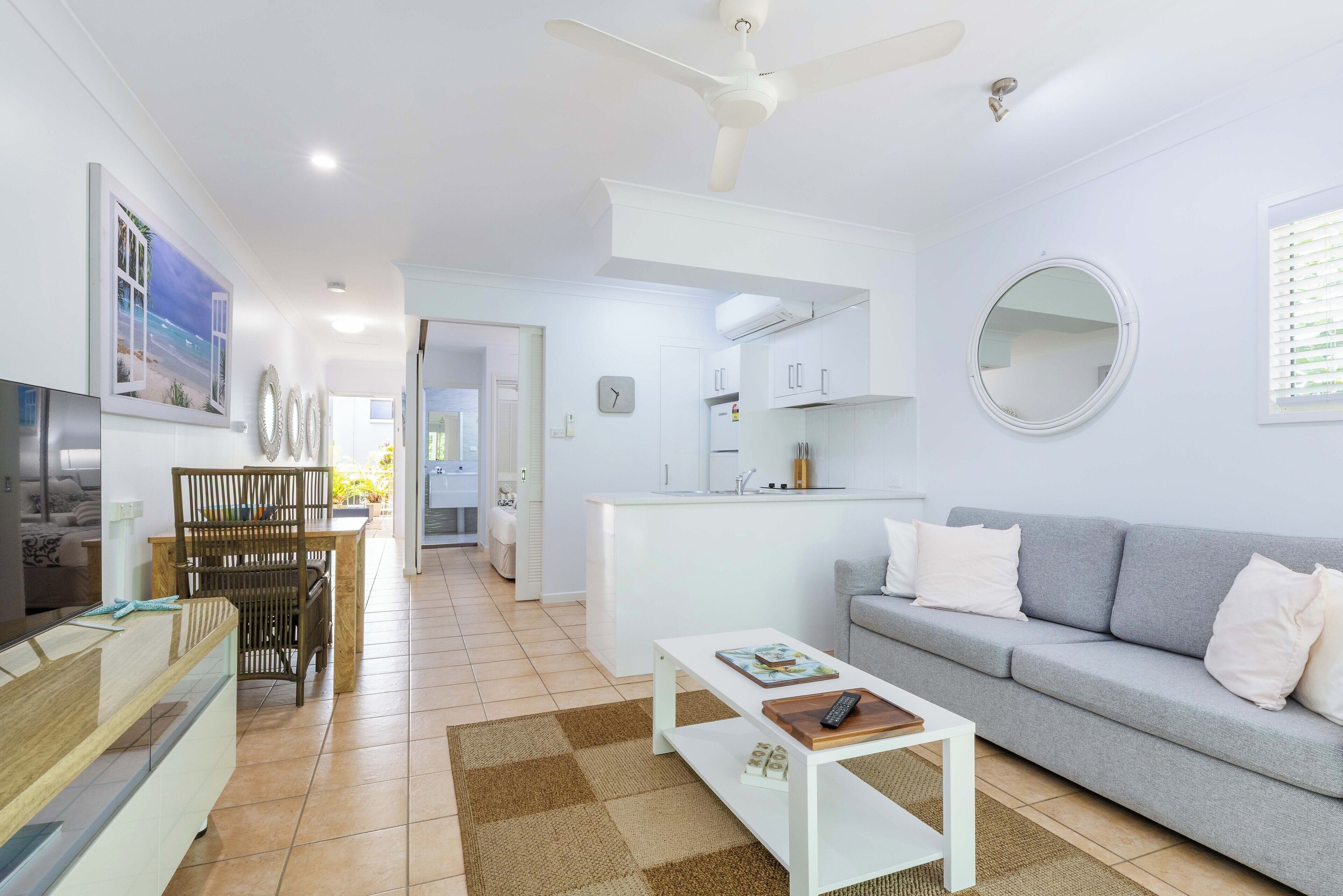 A modern living room with a grey sofa, a white coffee table, and a dining area with a wooden table and chairs.