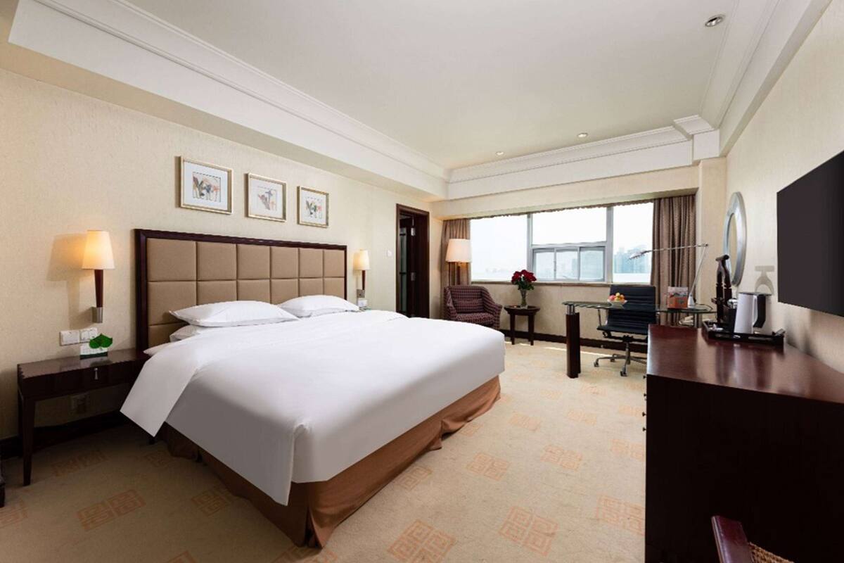 A hotel room with a large bed, a desk, a chair, a TV, and a window with a view.