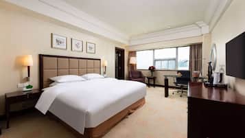A hotel room with a large bed, a desk, a chair, a TV, and a window with a view.