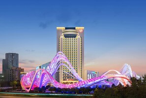 A modern hotel with a prominent tower and illuminated wave-like structures in front. - Ramada Plaza Wuhan Optics Valley (Wuhan)