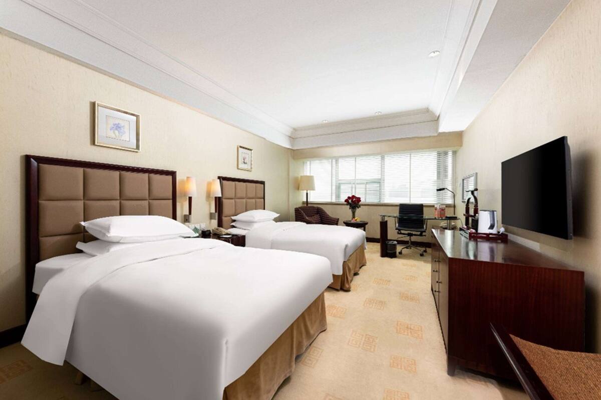 A hotel room with two beds, a desk, a chair, a television, and a window with blinds.
