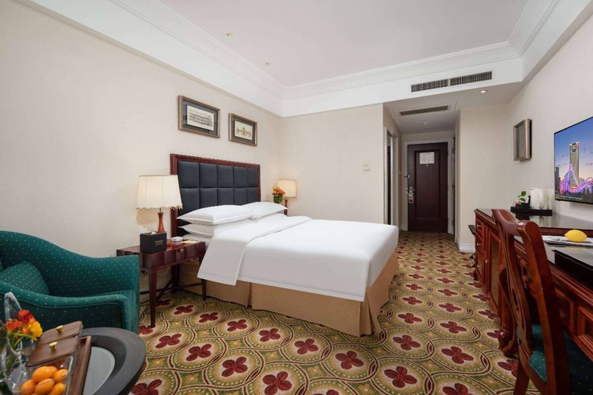 A hotel room with a large bed, a desk, a chair, a sofa, and a TV.