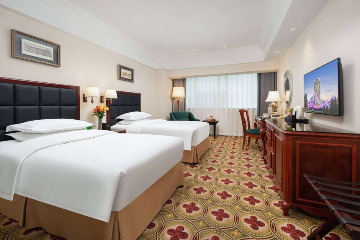 A hotel room with two beds, a desk, a chair, a TV, and a patterned carpet.