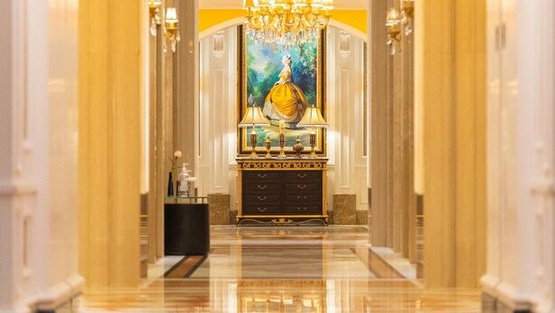 Um corredor luxuoso com um lustre imponente, um quadro decorativo e um conjunto de móveis dourados ornamentados.