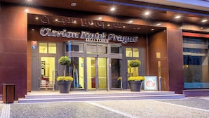 La entrada del Hotel Clarion Prague Old Town, con una fachada moderna, puertas de cristal grandes y plantas en macetas a la entrada.