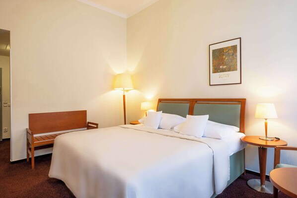 Habitación de hotel con una cama grande, dos mesitas de noche con lámparas, un banco de madera y un cuadro enmarcado en la pared.