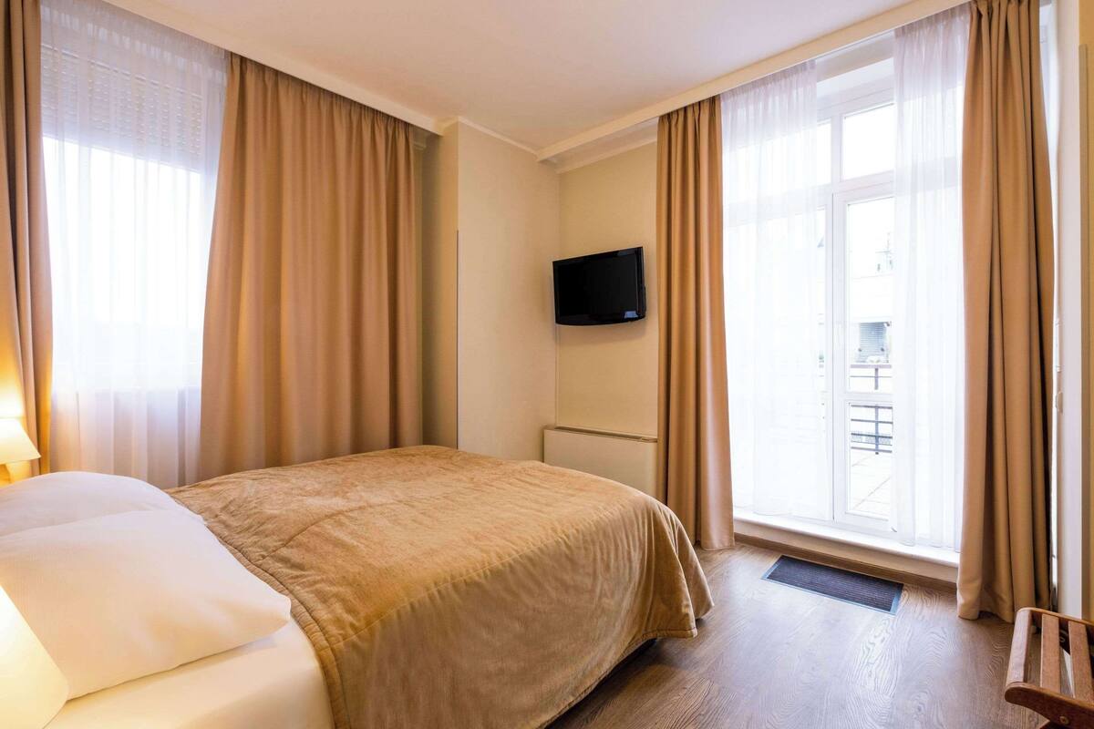 Een hotelkamer met een bed, een aan de muur bevestigde televisie en een raam met gordijnen.