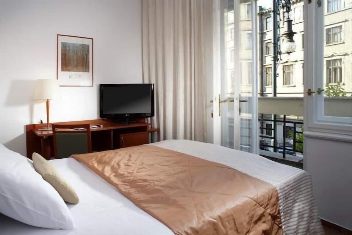 Een hotelkamer met een bed, een bureau met televisie, een raam met uitzicht op gebouwen en een deur.